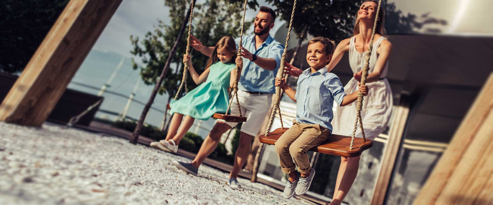 Happy Parents Pushing Their Children On A Swing