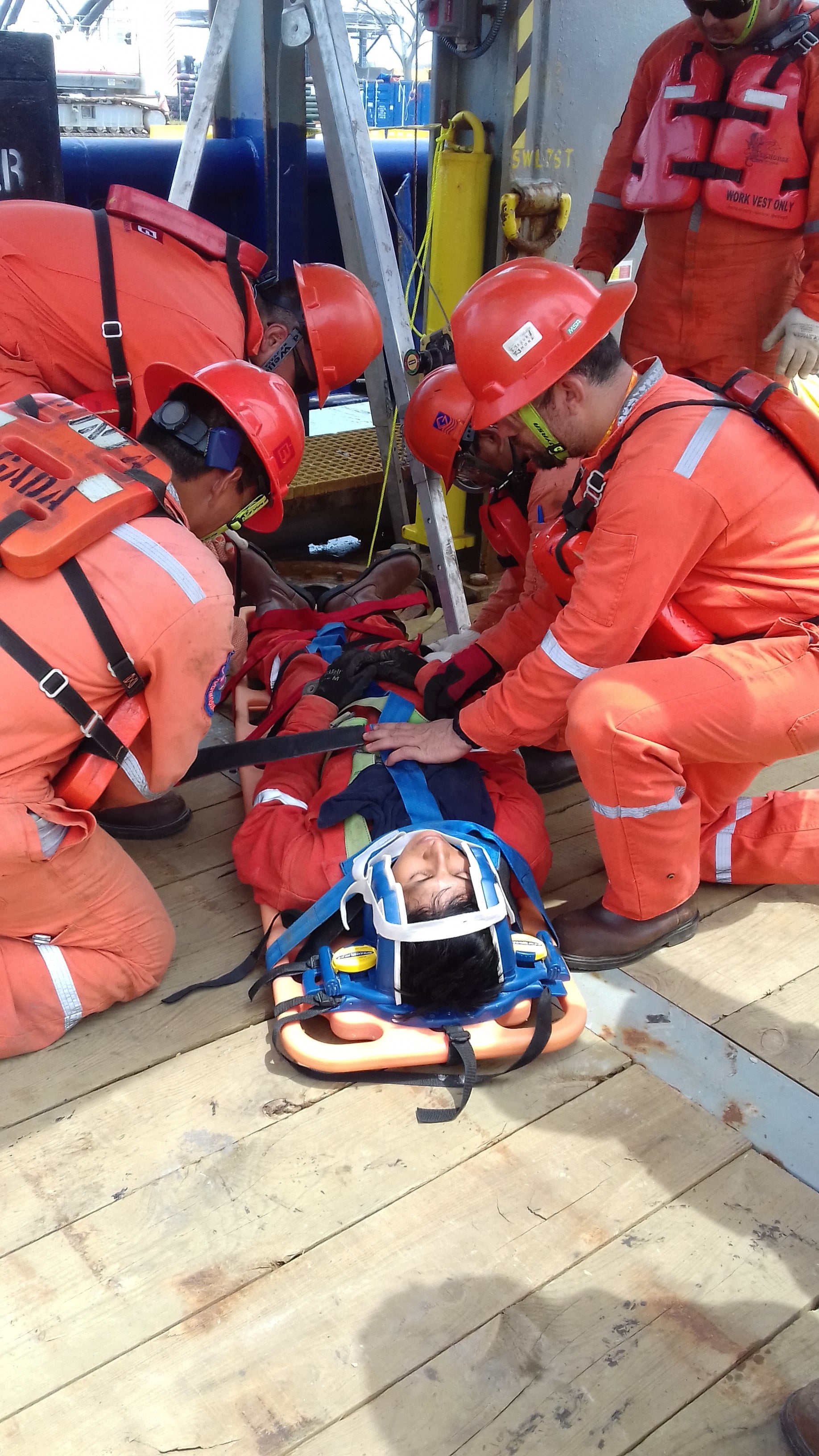 Emergency response team in orange safety gear tending to an injured person on a stretcher on a ship deck.