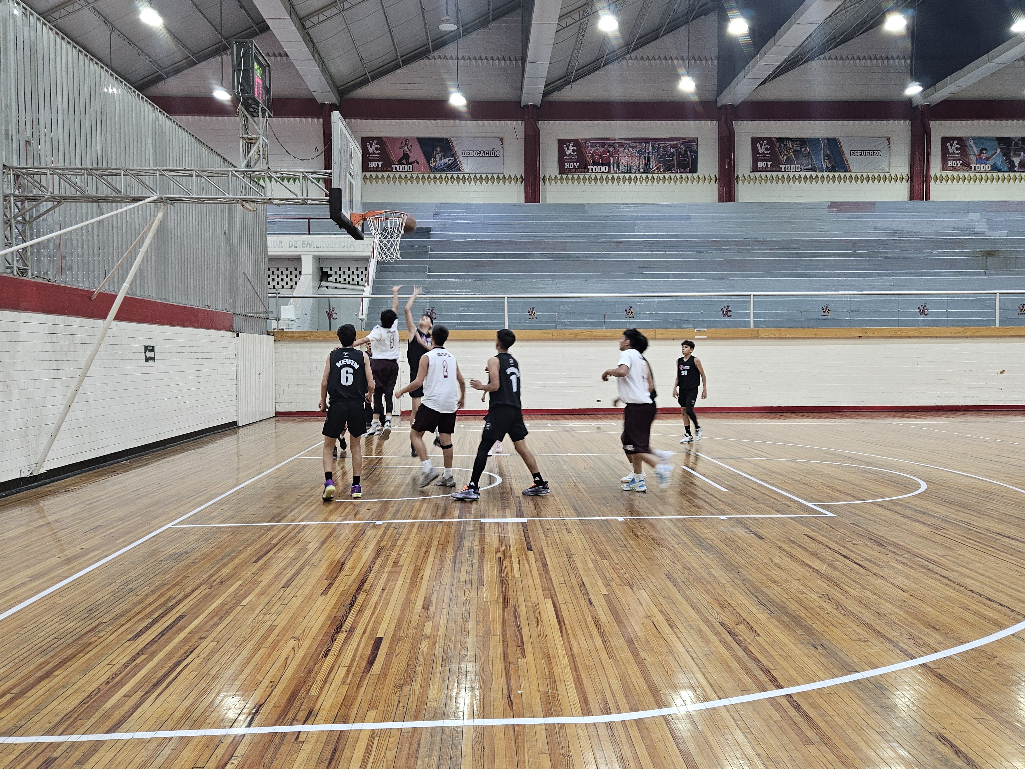 Interior de una arena de baloncesto vacía con asientos de colores y una cancha de juego.