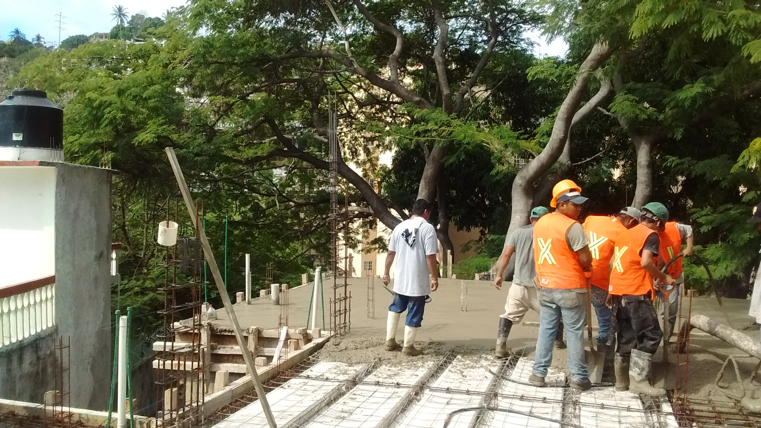 Trabajadores de la construcción vertiendo concreto en una obra al aire libre, rodeados de árboles. Trabajadores de la construcción vertiendo concreto en una obra al aire libre, rodeados de árboles.