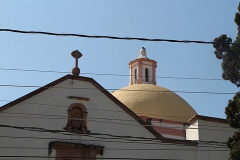 Cúpula de iglesia antigua contra cielo azul con árboles y cables eléctricos visibles.