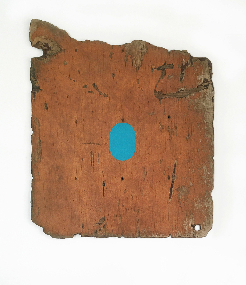 A large piece of distressed painted plywood with a turquoise oval in the center.