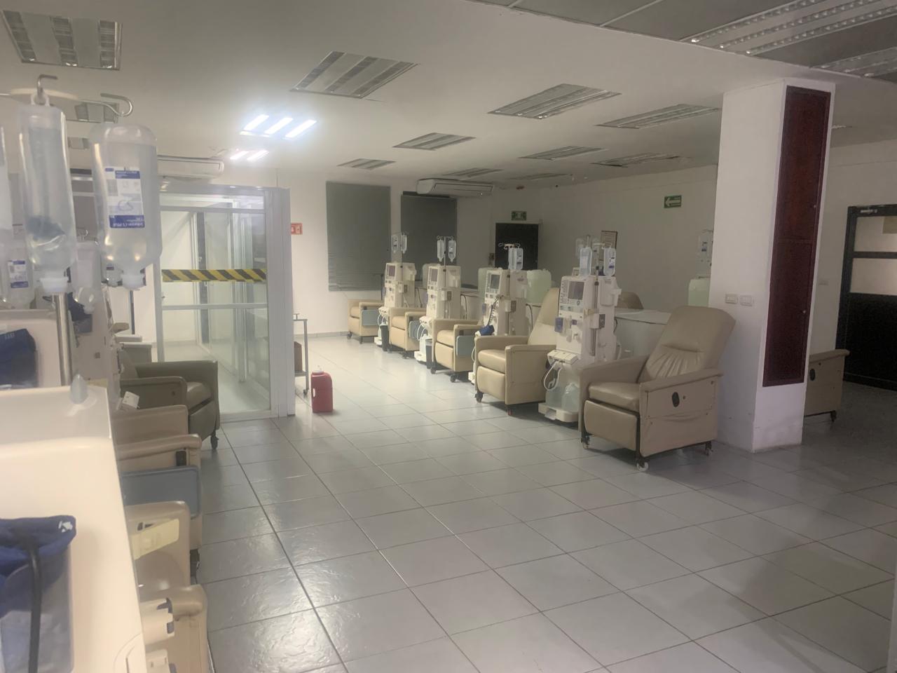 Sala de tratamientos vacía con sillas reclinables y máquinas de diálisis.