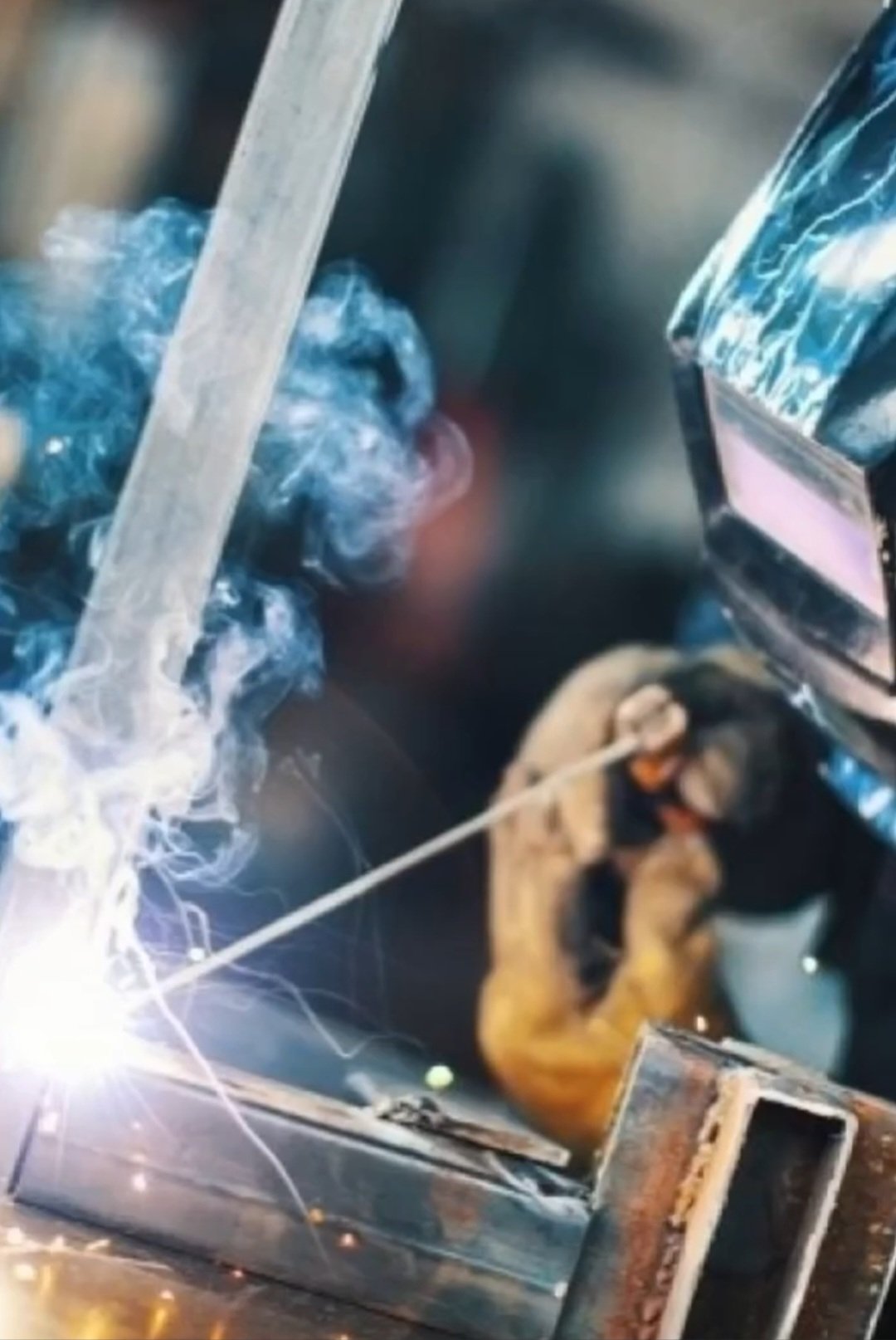 Person in protective gear performing arc welding with sparks and smoke.