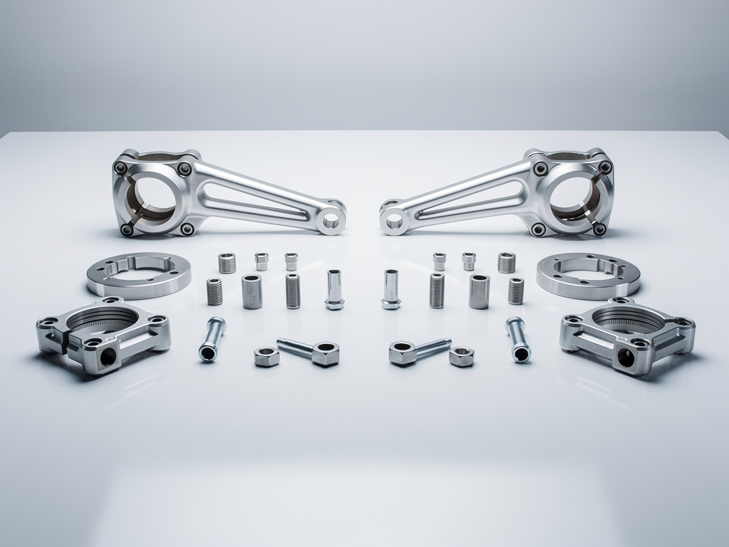 Kit de piezas metálicas mecanizadas con soportes, anillos, tornillos y tuercas sobre superficie blanca