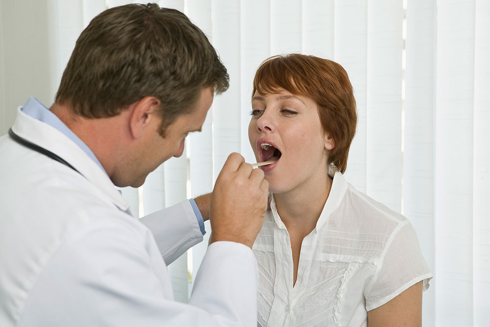 Doctor revisando la garganta de una paciente en una consulta médica.