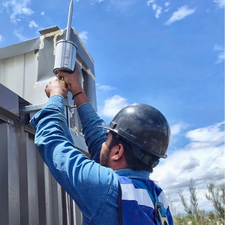 Dos personas en una plataforma elevadora trabajando en un edificio industrial bajo un cielo despejado.