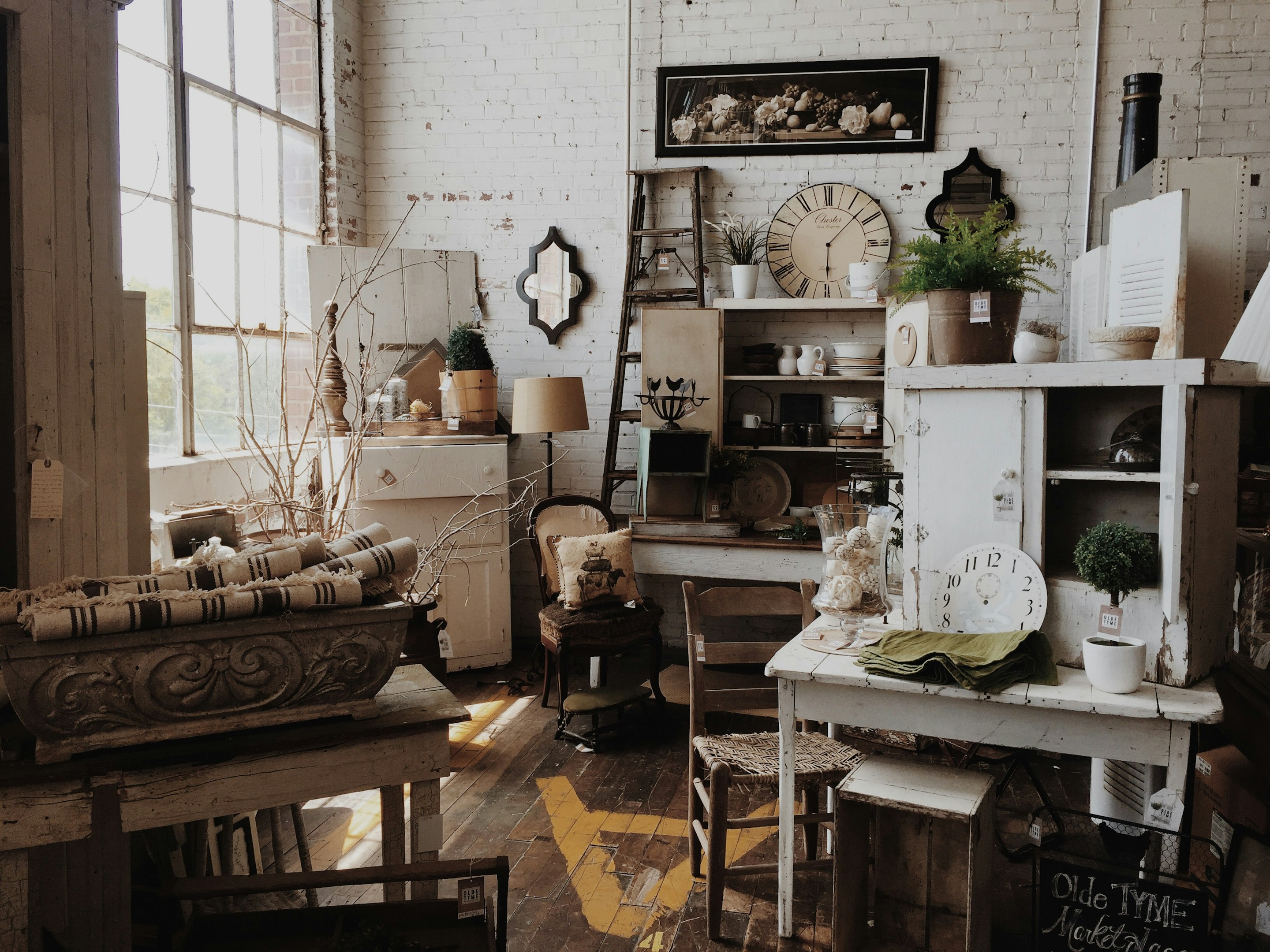 Elegant kitchen view through open wooden doors, featuring a central island, hanging chandelier, framed artworks, a large rug, and a potted plant.
