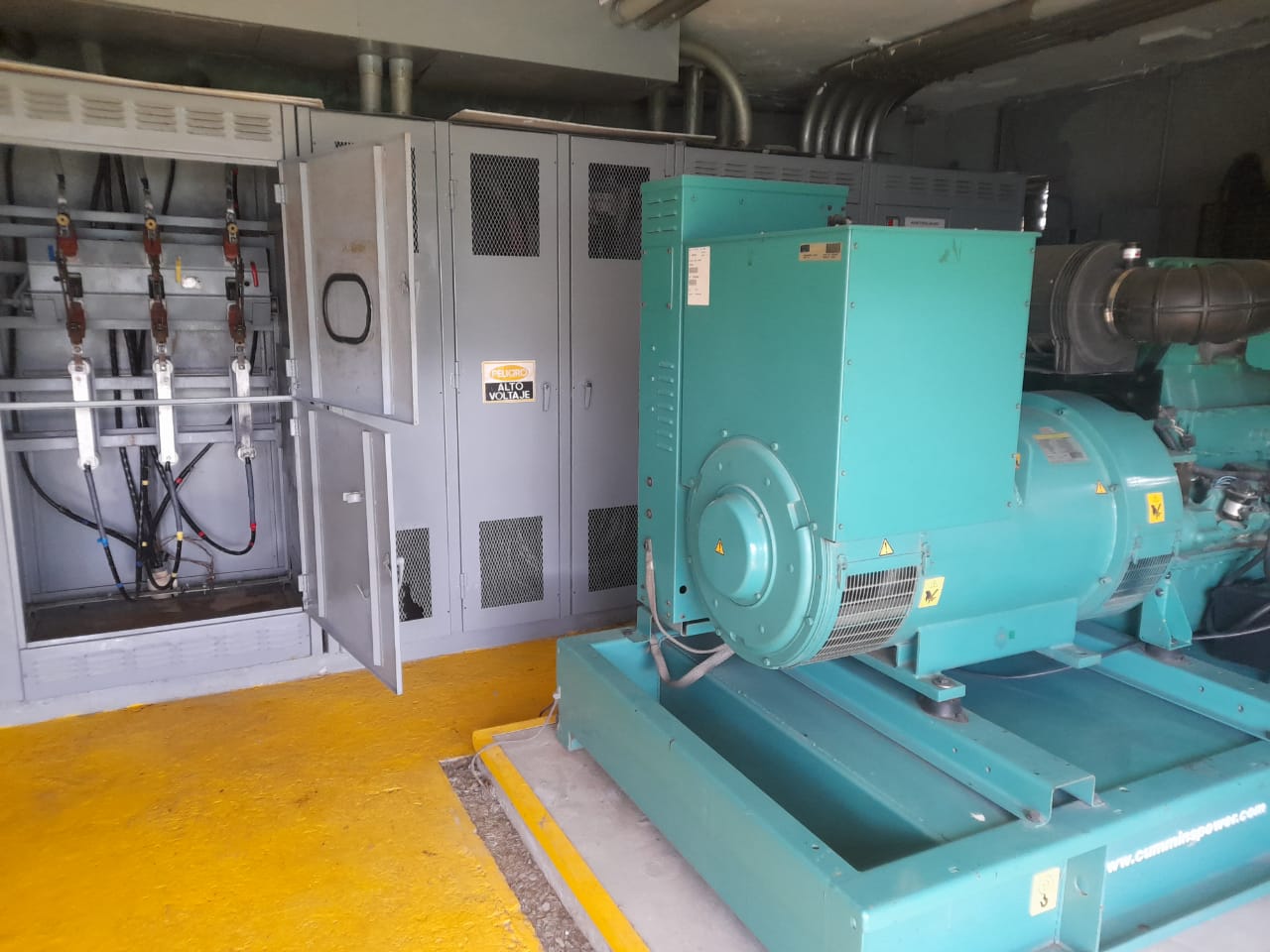 Generador eléctrico industrial turquesa junto a paneles de alto voltaje en sala de máquinas