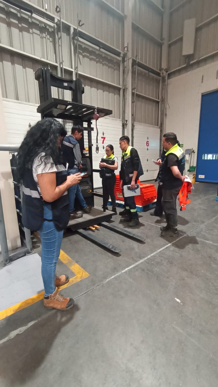 Grupo de personas con uniformes de seguridad alrededor de una carretilla elevadora en un almacén.