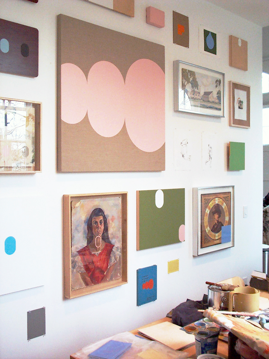 Colorful modern paintings and drawings on a wall behind an artist’s worktable.