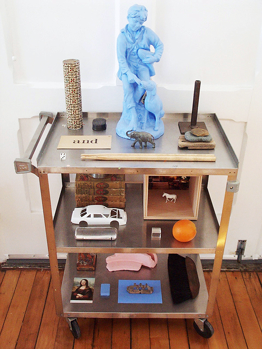 A utility cart with objects on it, including a blue painted statue of a boy and dog.