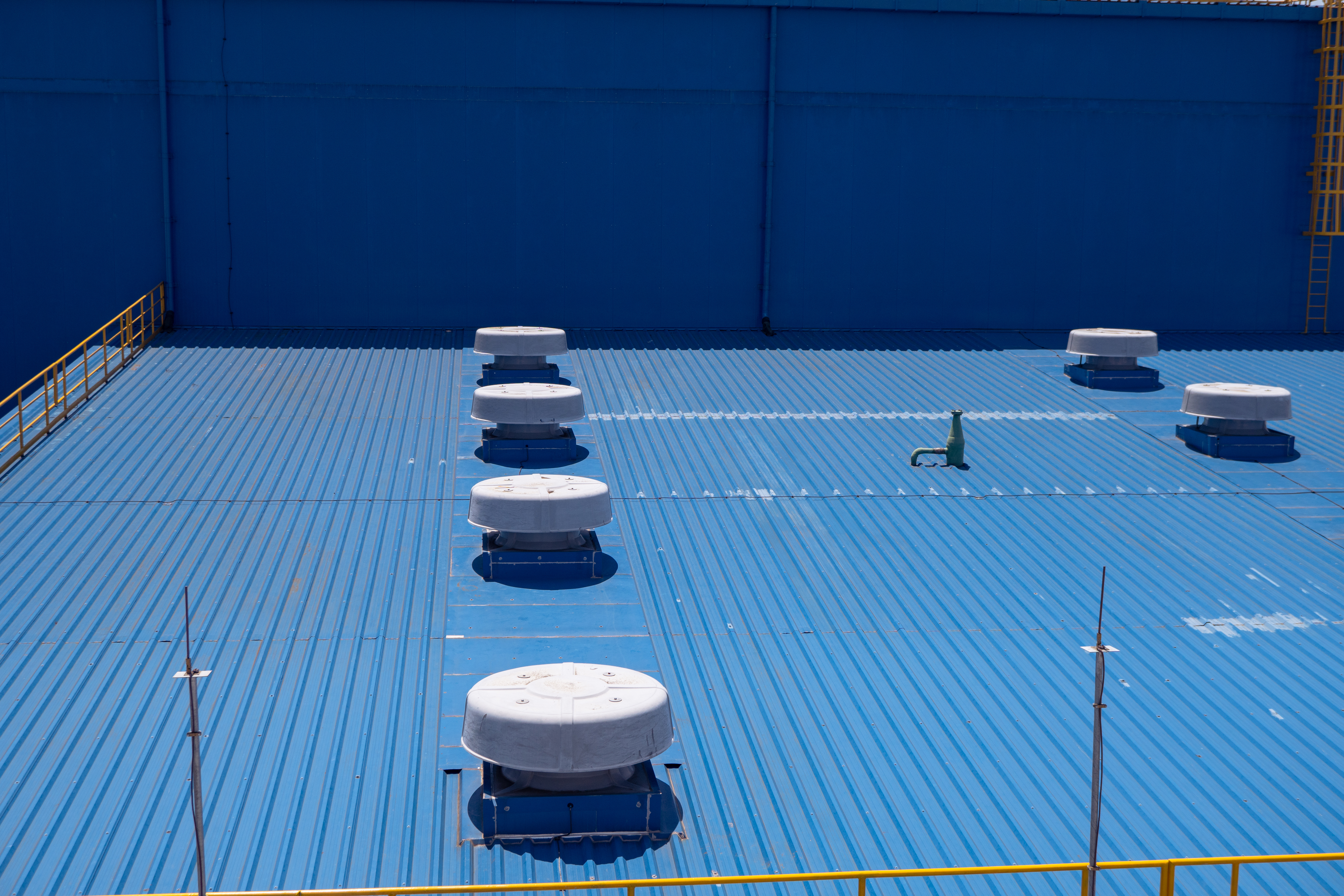 Blue industrial metal roof with white ventilation units and yellow safety railings