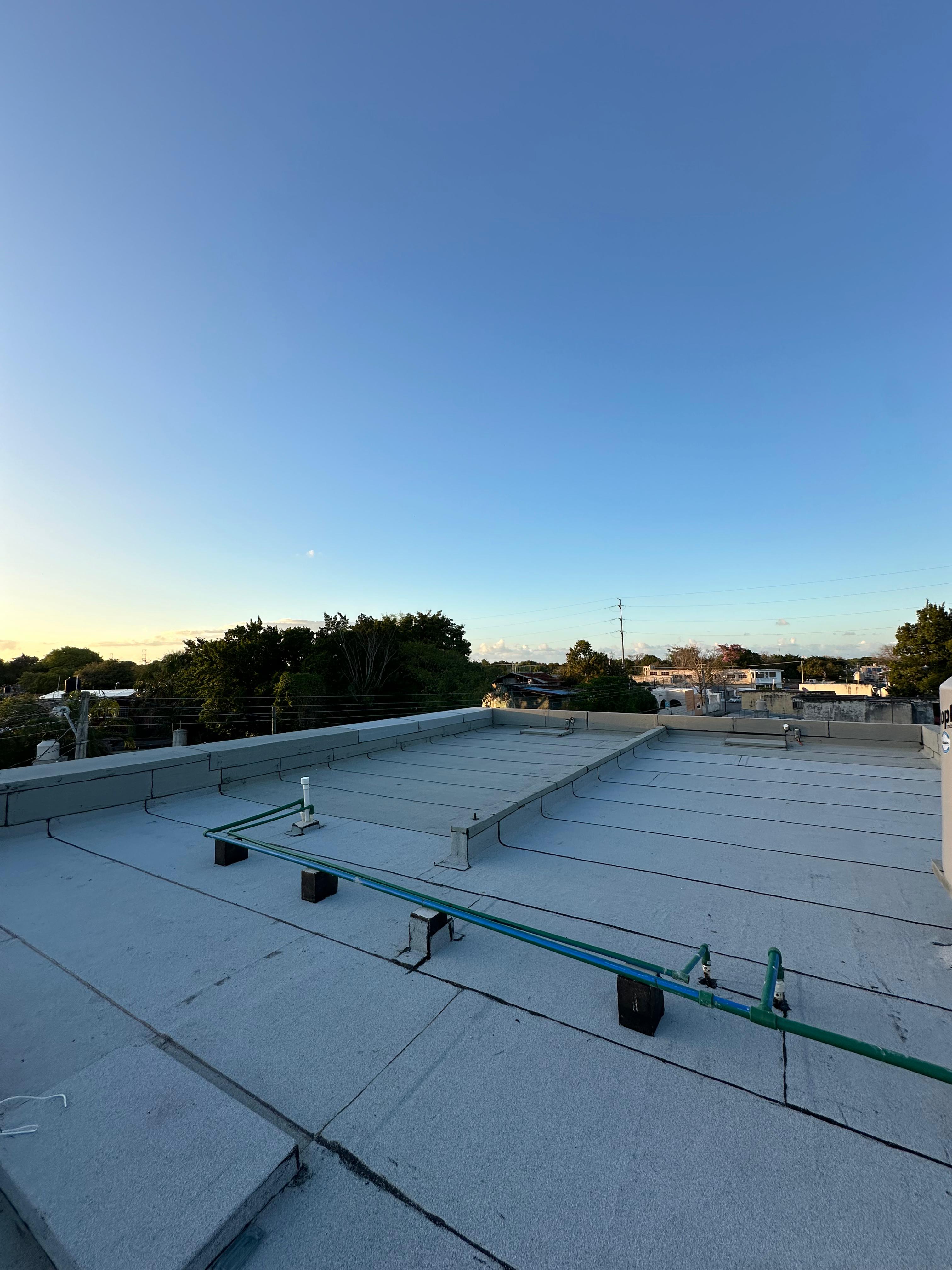 Techo plano de concreto con cielo despejado y vista a un vecindario en la distancia.