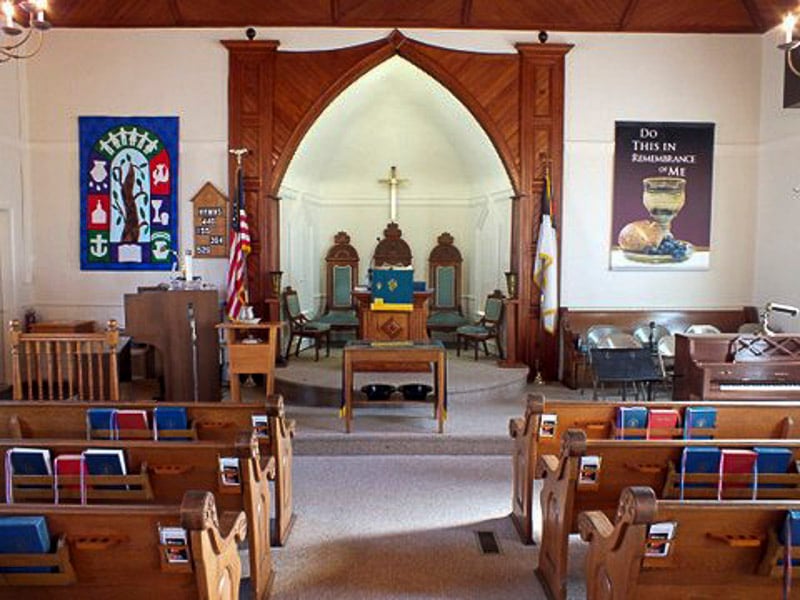 Congregation seated in a church facing the altar with a large cross and stained-glass window.
