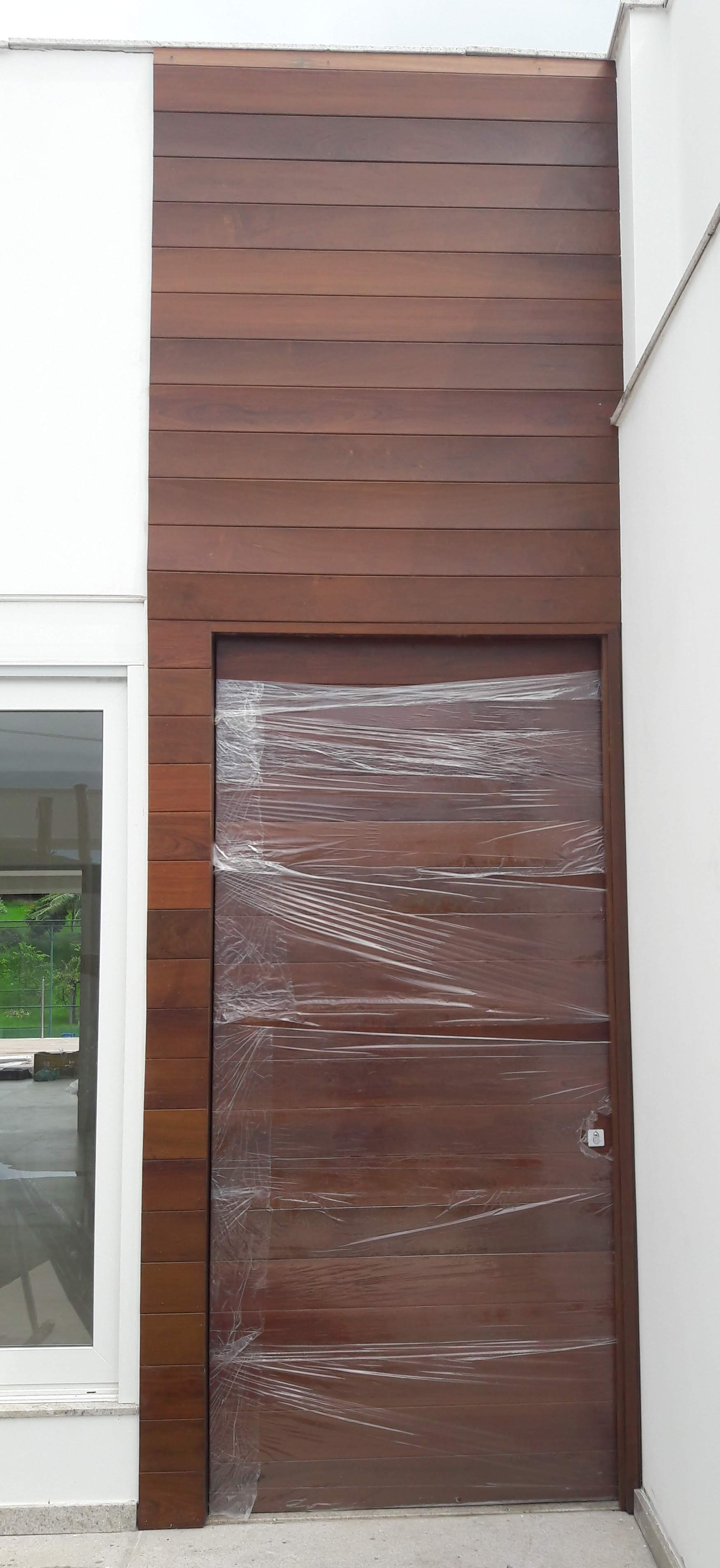 Porta de entrada em madeira, pivotante e painel em madeira.