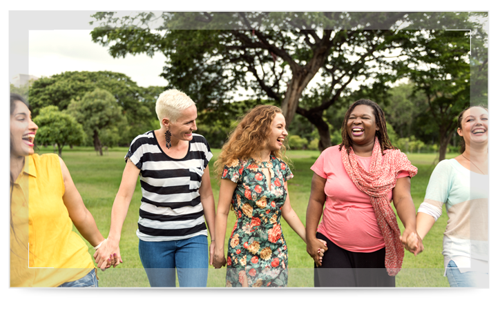 Three senior women holding hands and laughing in the sun