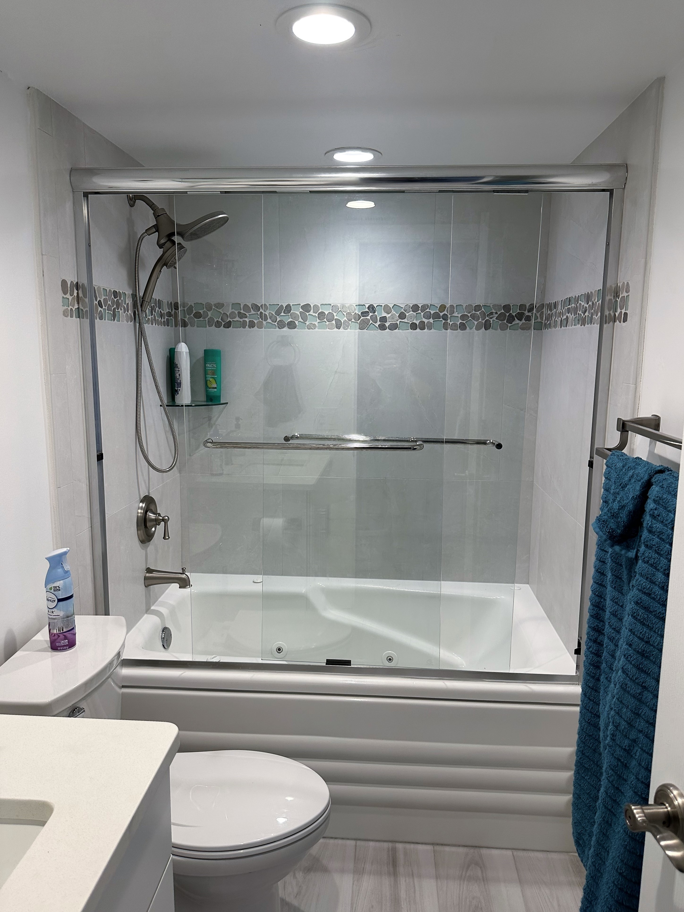 Large bathtub and shower combo featuring Oyster Bay shaved pebble bands with by-passing semi-frameless shower doors.