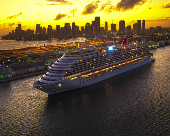 A Carnival cruise ship leaving port at sunset.