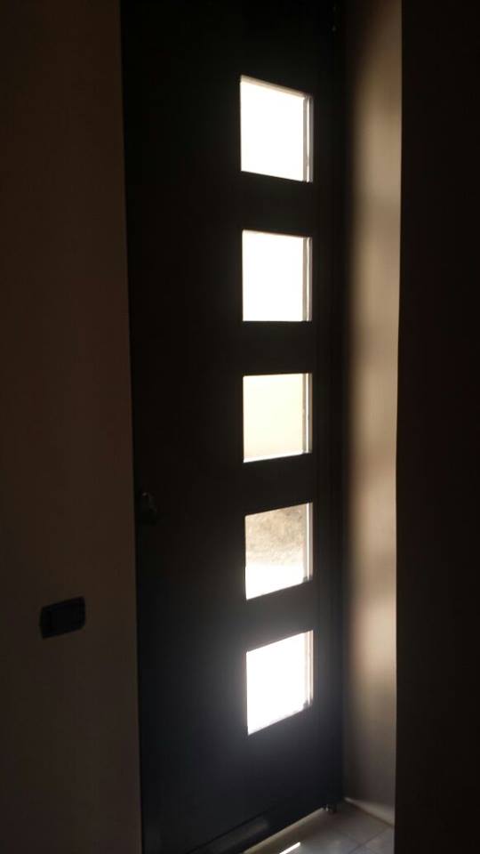 Puerta de aluminio color bronce con detalles de vidrio a lado.