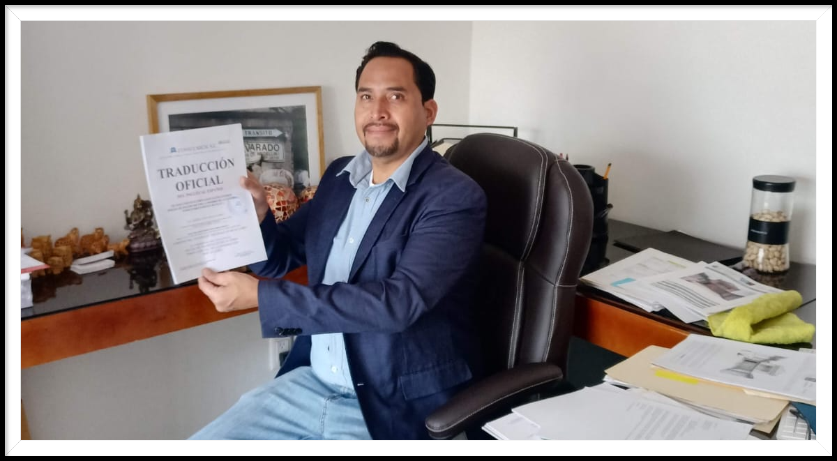 Hombre en oficina sosteniendo un documento de traducción oficial, con mesa llena de papeles y objetos decorativos al fondo.