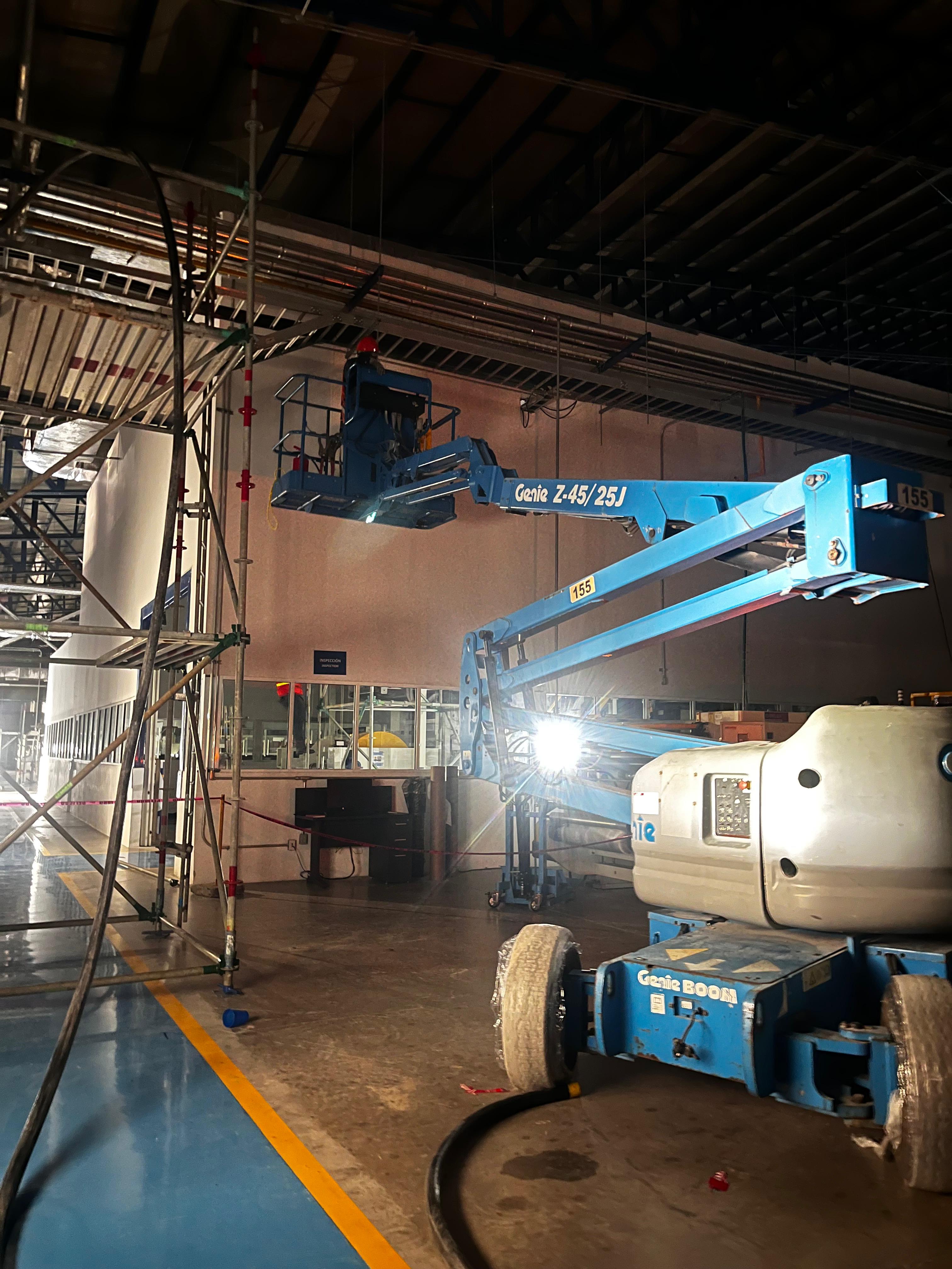 Elevador azul Genie Z-45/25J en un almacén industrial con una persona trabajando en altura.