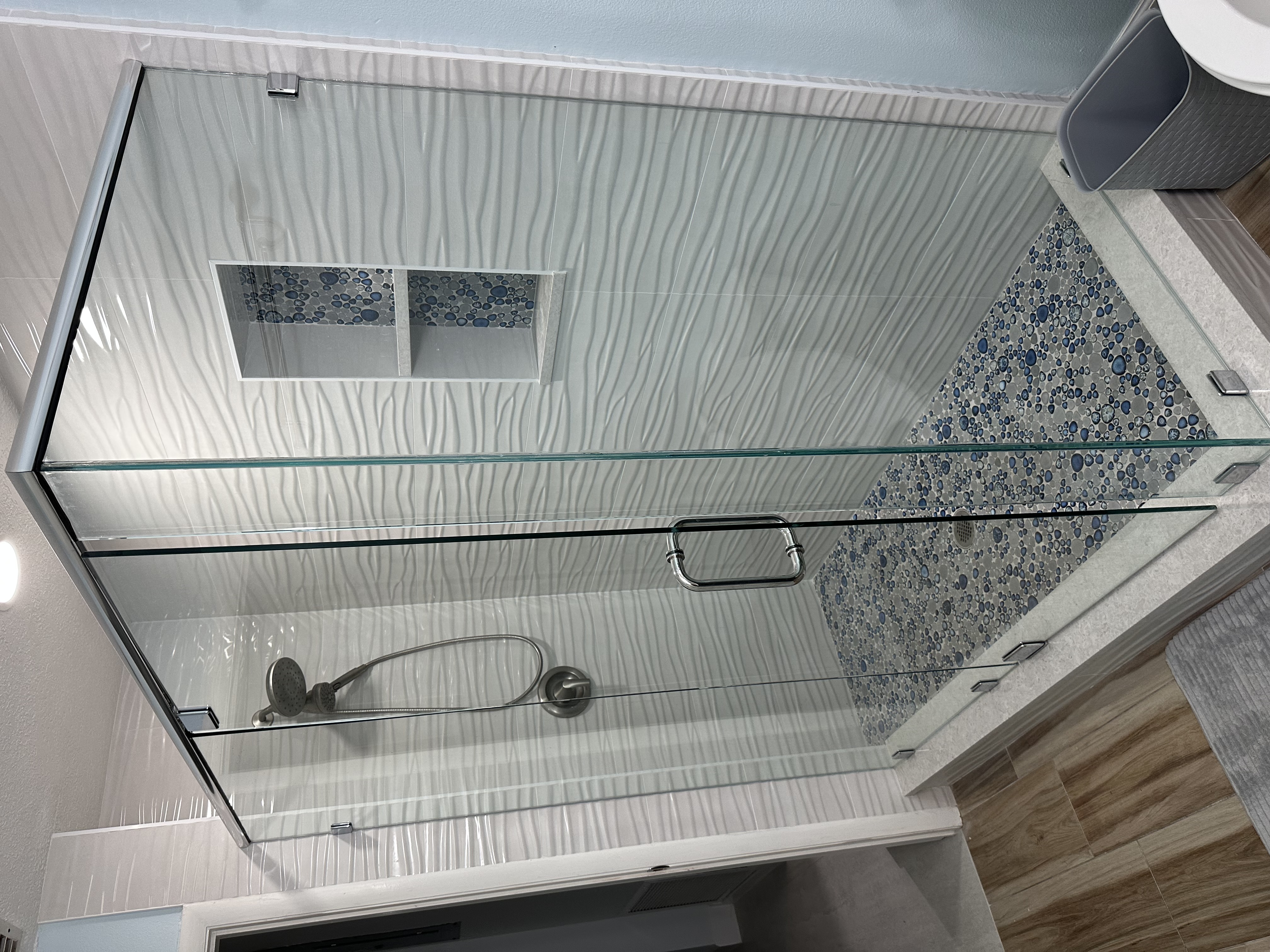 This beautifully tiled shower, enclosed in heavy clear glass, combines white wavy walls
with a blue-grey porcelain mosaic floor and dual niches—creating a calm, pristine retreat for everyday luxury.